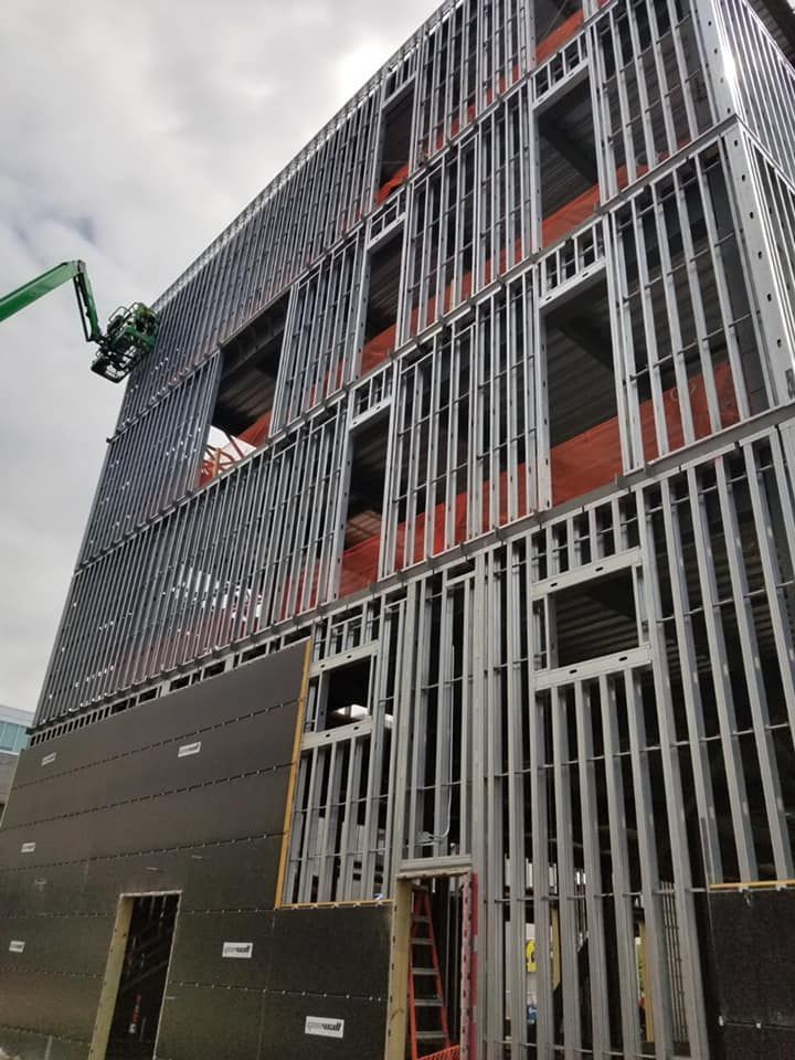 Steel frame of a building under construction; window openings, brown material visible, cloudy sky.