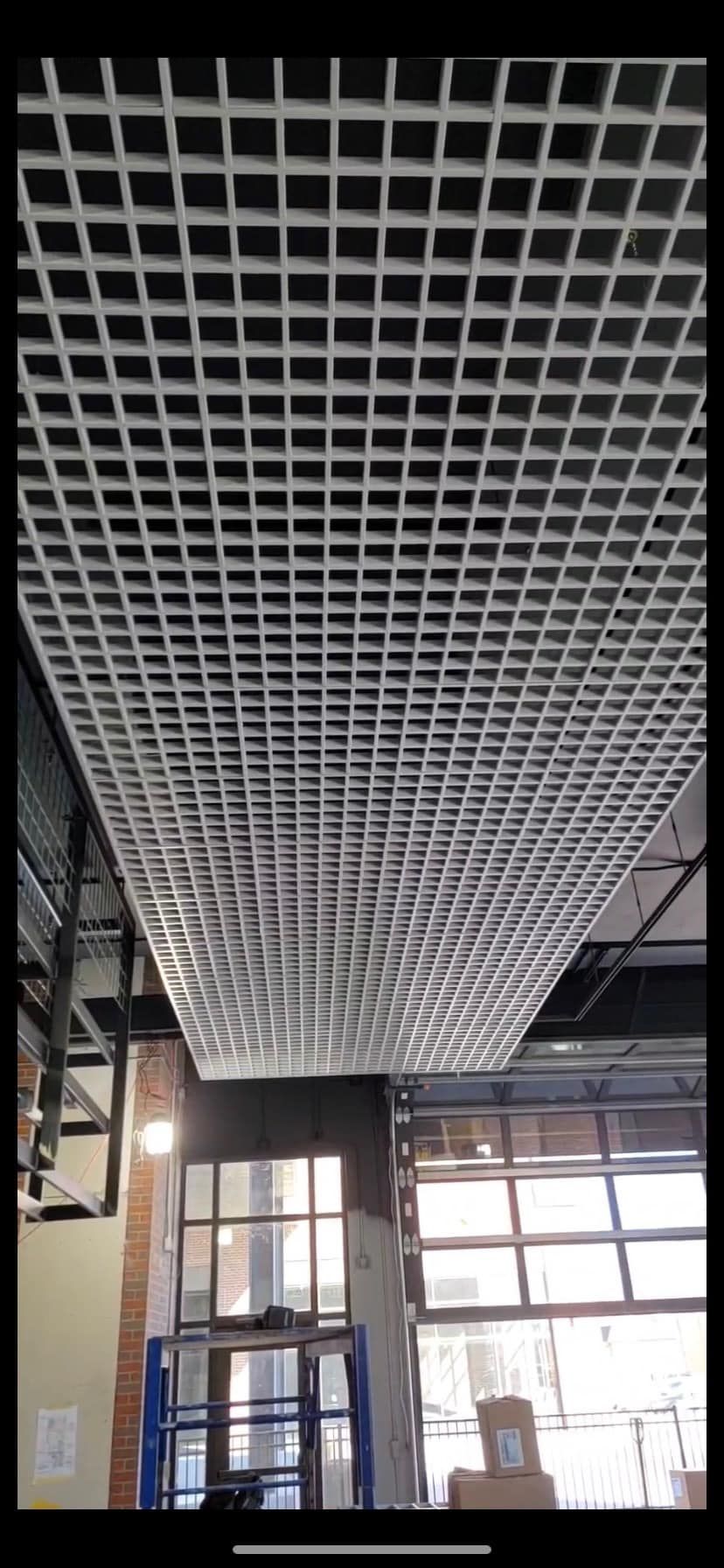 Grid ceiling in a modern space. Brick wall, windows, and construction lift visible.