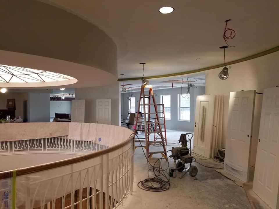 Interior construction site; curved railing, ladder, unfinished walls, hanging lights.