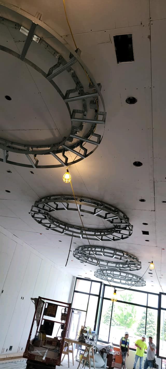 Construction site with circular metal structures in the ceiling. Workers near windows and a lift.