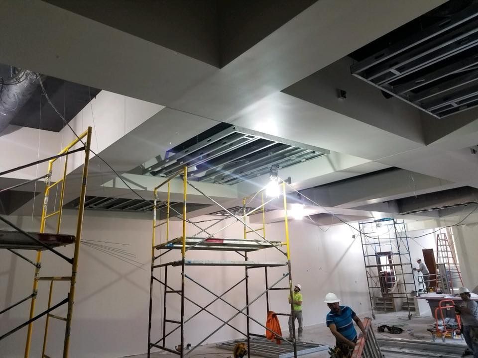 Construction site with scaffolding, workers, and unfinished ceiling with exposed metal.