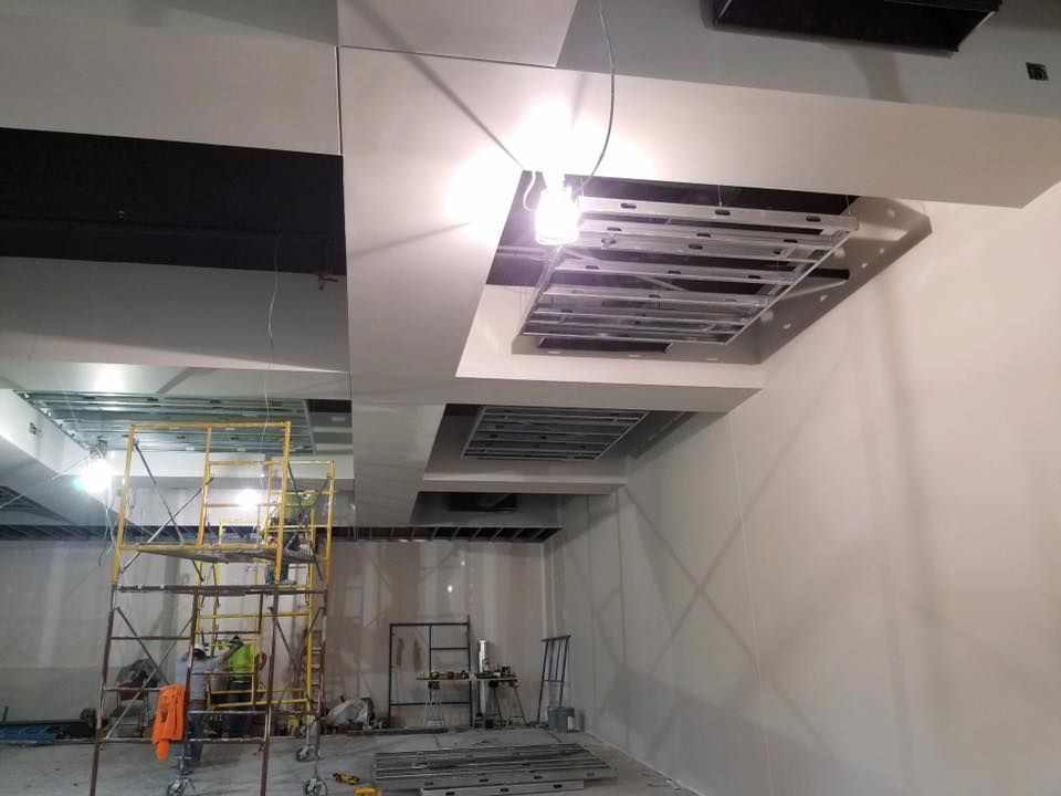 Construction site: Workers on scaffolding installing ceiling panels in a white-walled room.