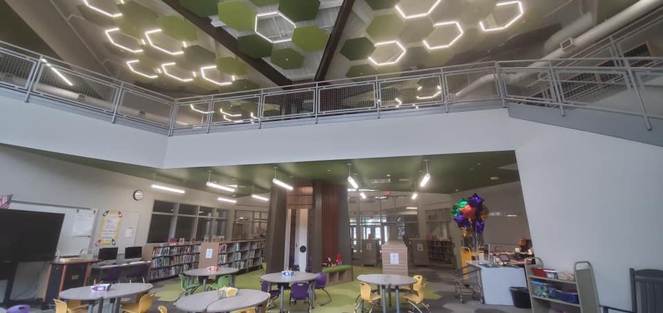 A library with a mezzanine level and a honeycomb ceiling design, tables, and bookshelves.
