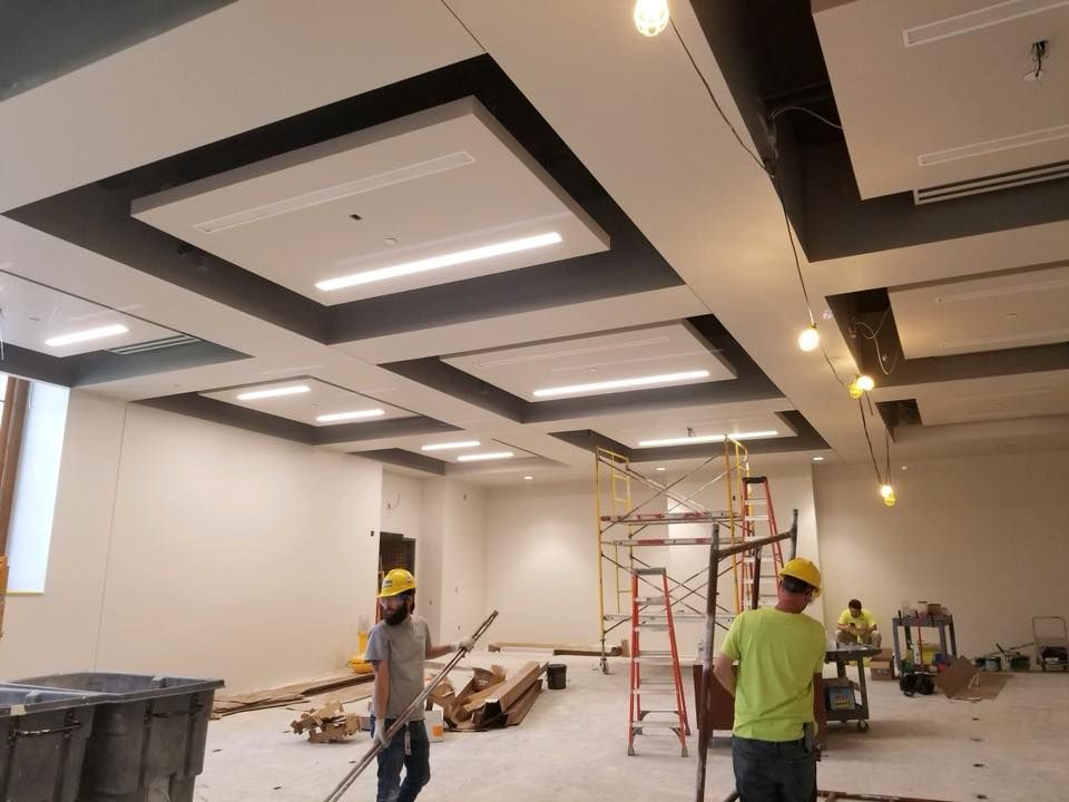 Construction workers in room, installing ceiling with inset lighting; white walls and black accents.