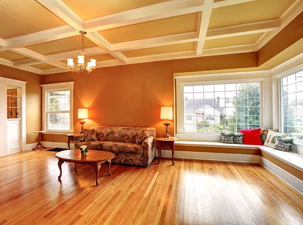 Living room with wooden floor and ceiling. Tan walls, floral sofa, bay window with bench seat, and chandelier.