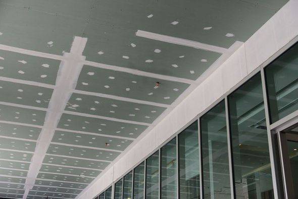 A partially finished ceiling with drywall taped and mudded, above a glass-walled building facade.
