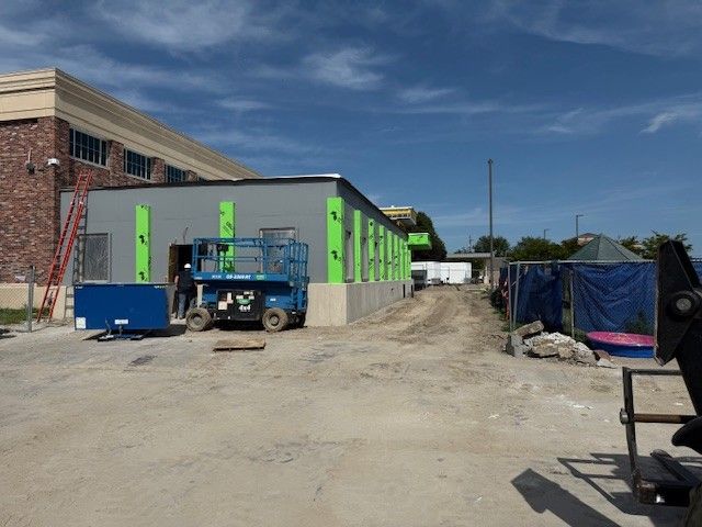Construction site: blue lift and building with green boards, person working, sunny day.