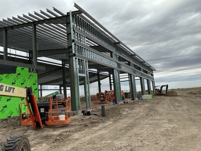 Construction site with steel framing. Building under construction, green insulation, heavy machinery, cloudy sky.
