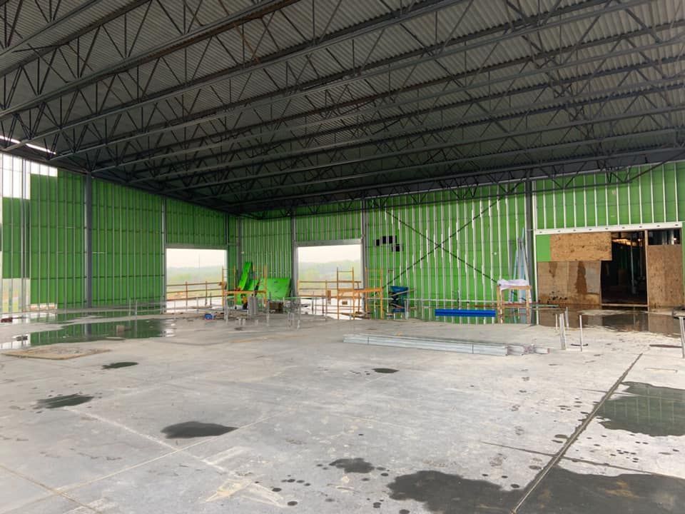 Construction of an empty warehouse interior, featuring metal studs, exposed roof beams, green insulation, and concrete floor.