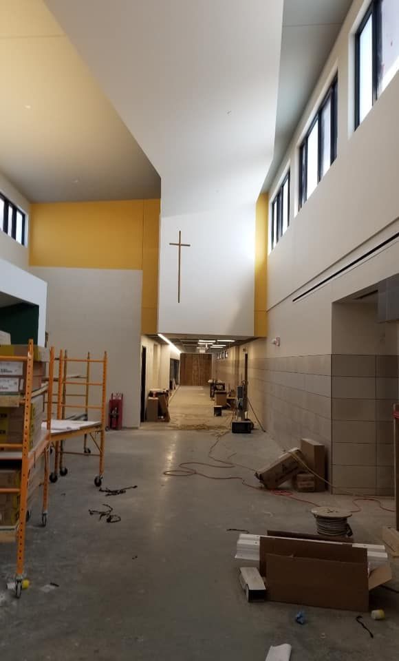 Interior of a building under construction; white walls, cross, gold accent wall, windows along the right, and debris.