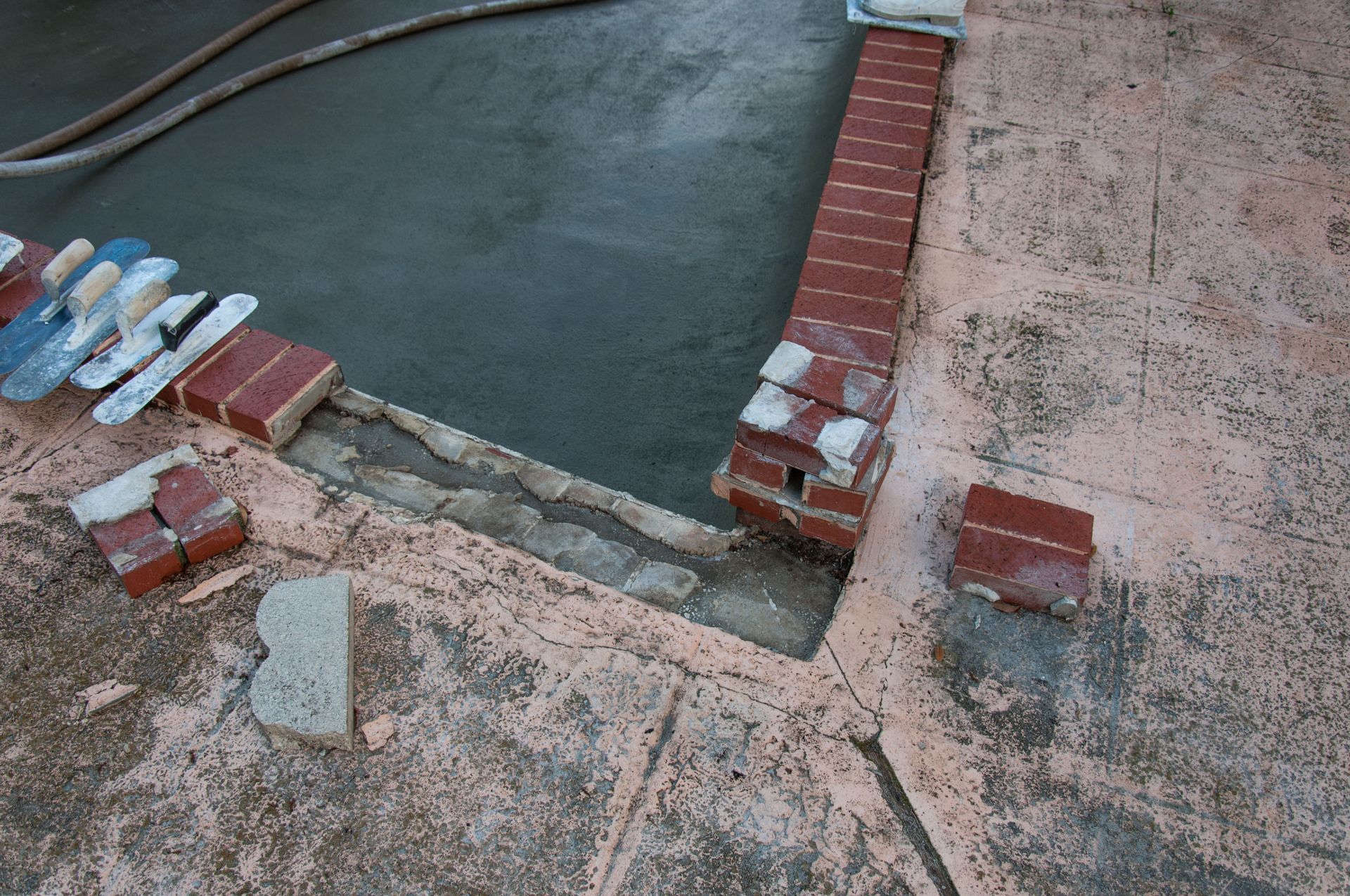 Partially built brick-lined pool edge with wet concrete and stacked materials nearby