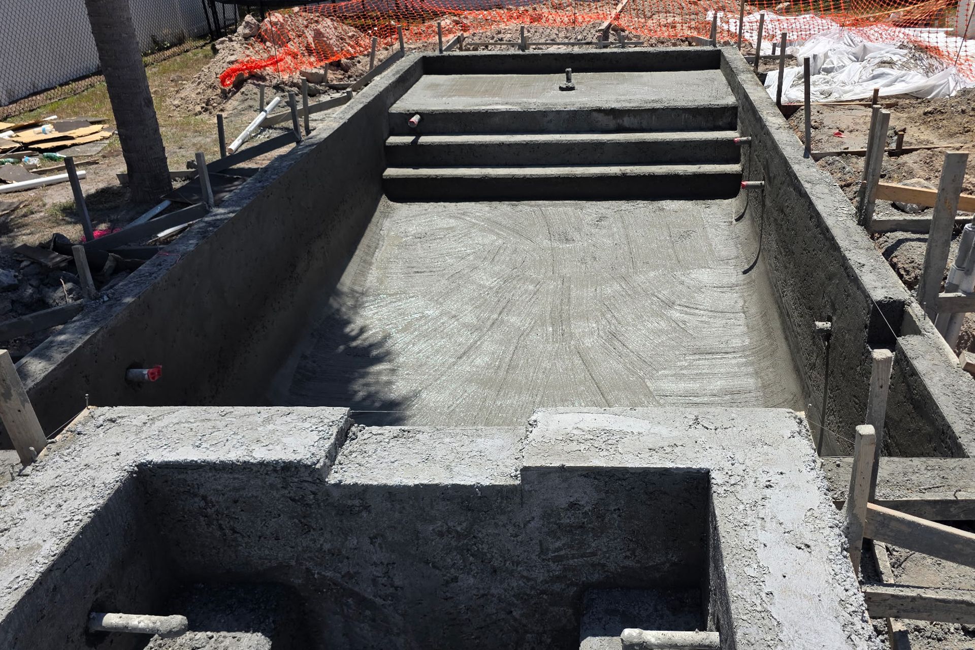 Concrete steps and a ramp under construction beside a retaining wall and orange safety fencing.