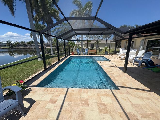 Screened backyard pool with tan patio and palm trees overlooking the water