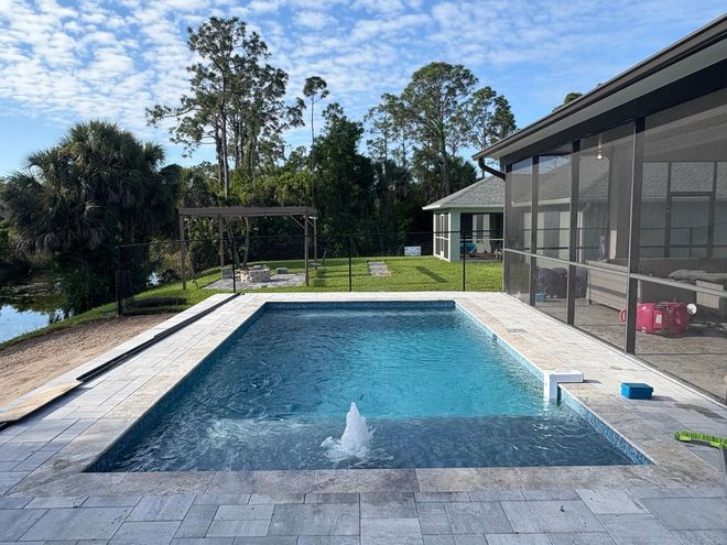 Modern backyard pool beside a screened house, with lake view and patio under a blue sky