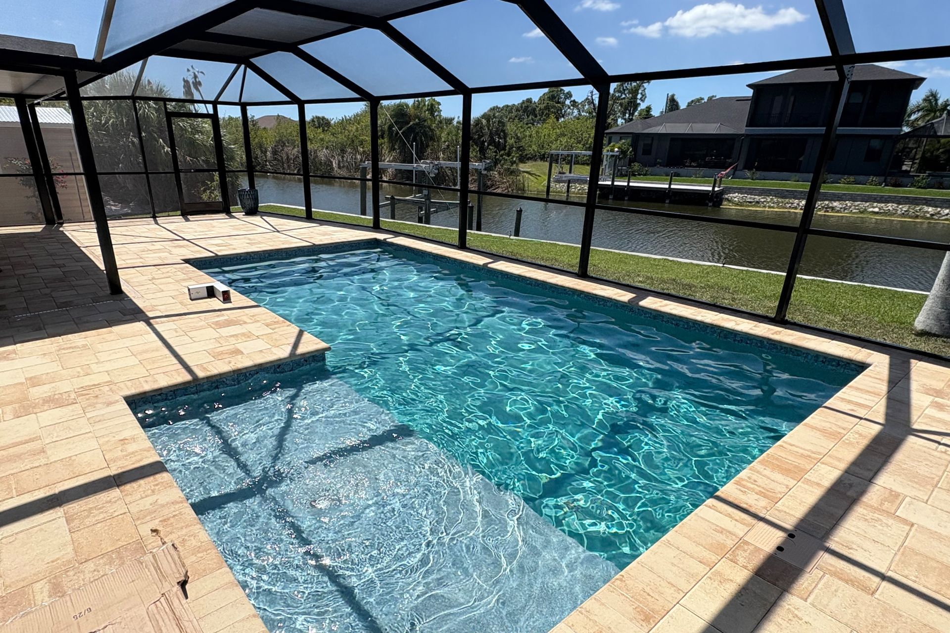 Screened-in backyard pool with turquoise water and a stone deck under a sunny sky