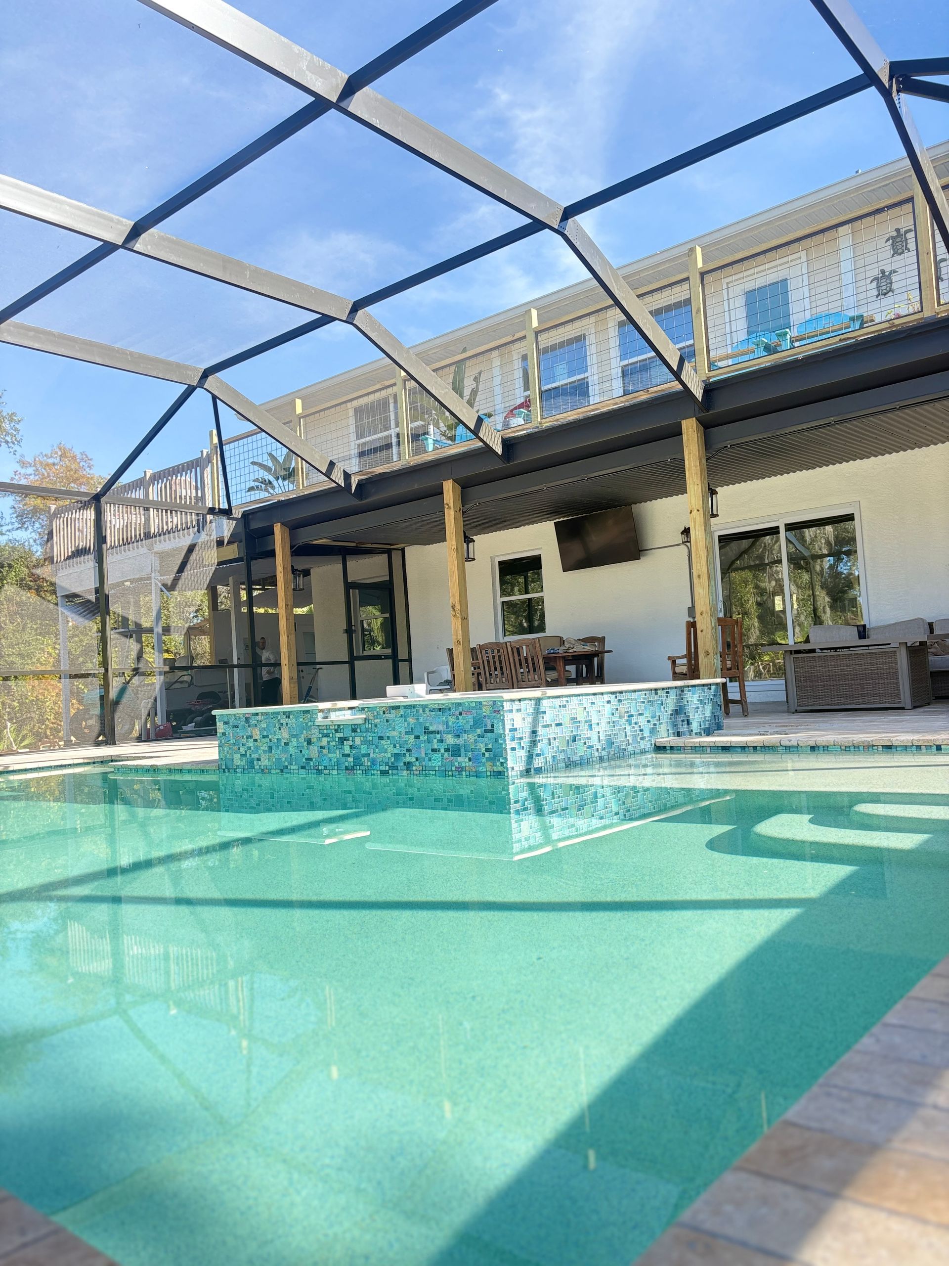 Backyard pool with turquoise water, covered patio, and screened enclosure under a blue sky
