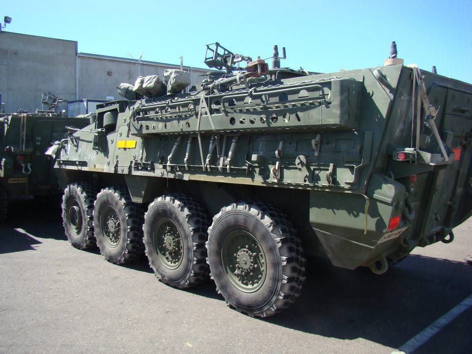 Green military armored vehicle with eight wheels parked outdoors in a lot