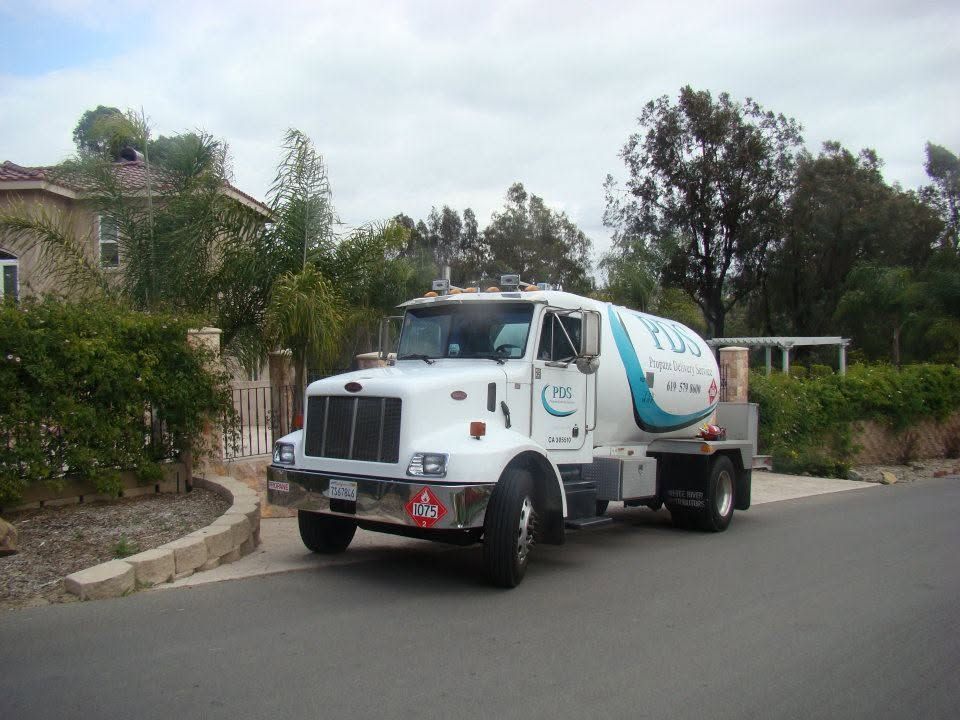White cement mixer truck parked on a street beside greenery and houses