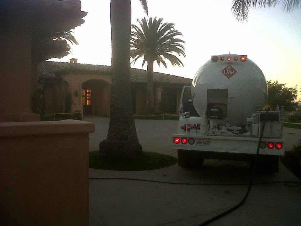 Tank truck parked on a driveway beside a stucco building and palm trees at sunset.