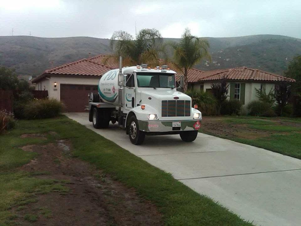 White cement mixer truck on a driveway in front of suburban houses, with hills in the background