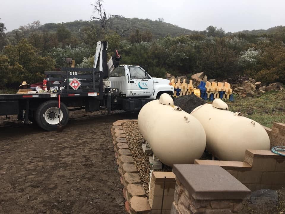 Truck beside large cream-colored tanks at a muddy worksite near rocky hills