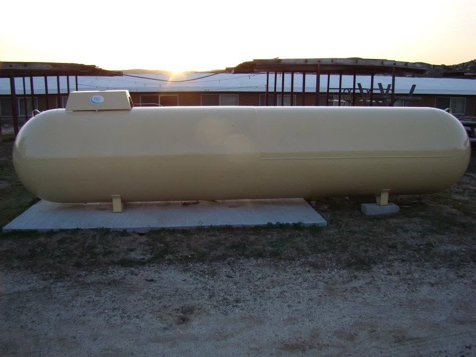 Large beige cylindrical tank on concrete pads outdoors at sunset.