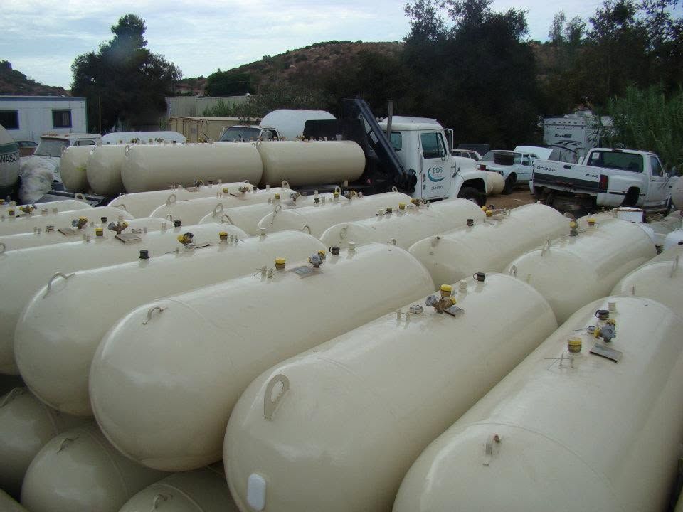 Rows of large white cylindrical tanks stored outdoors in an industrial yard, with trucks in the background