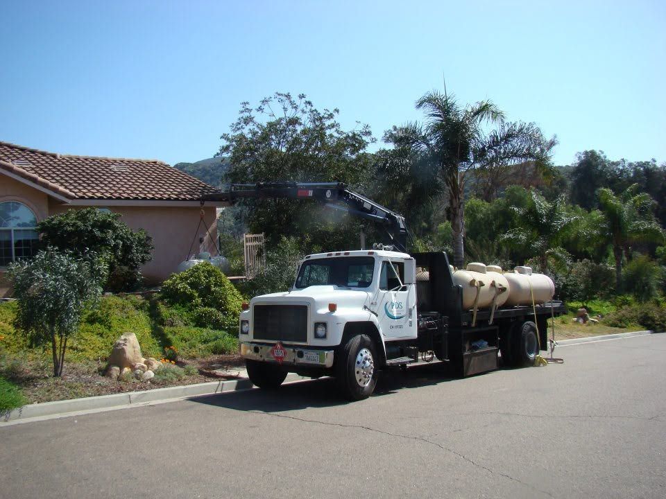 White tanker truck parked on a sunny suburban street beside a house and palm trees
