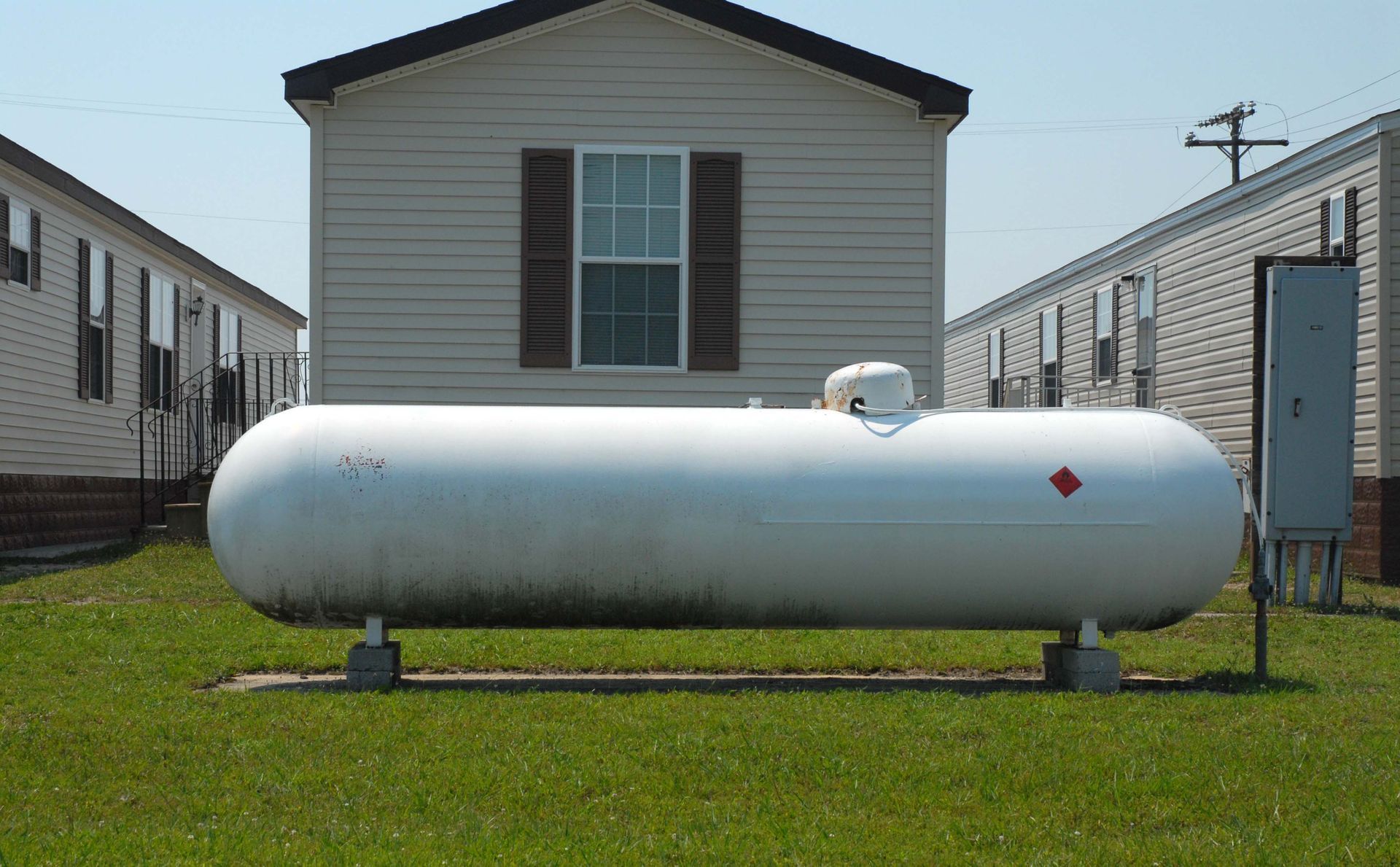 White propane tank in a grassy yard in front of a beige house with brown shutters