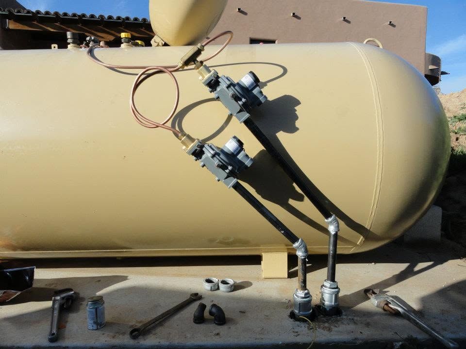 Two metal mechanical arms attached to a tan cylindrical tank outdoors, with tools on the ground.