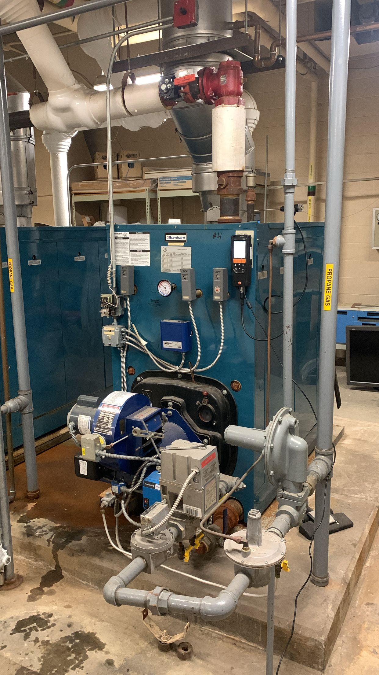 A large blue boiler is sitting in a room surrounded by pipes.