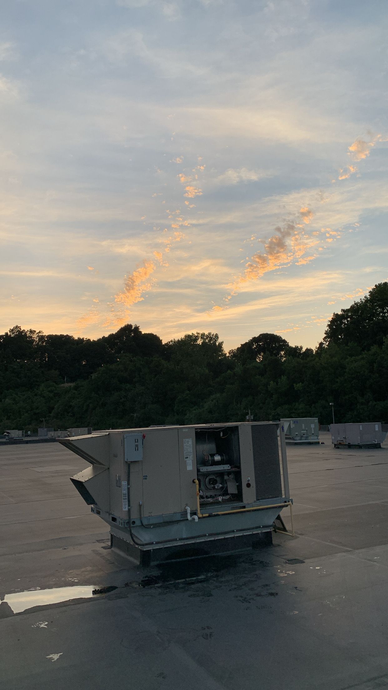 A large air conditioner is sitting on top of a roof at sunset.