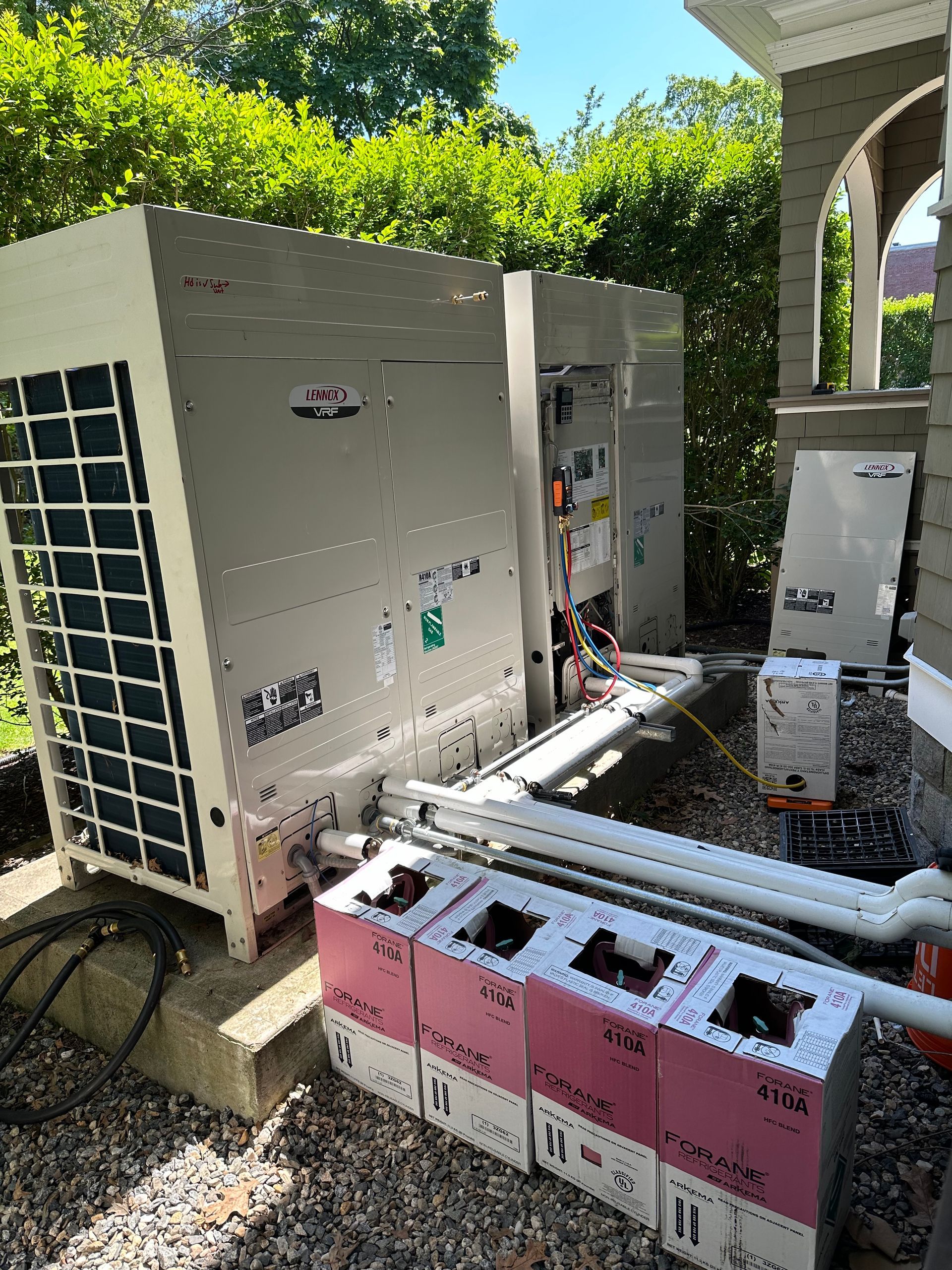 A large air conditioner is sitting on top of a gravel lot next to a house.