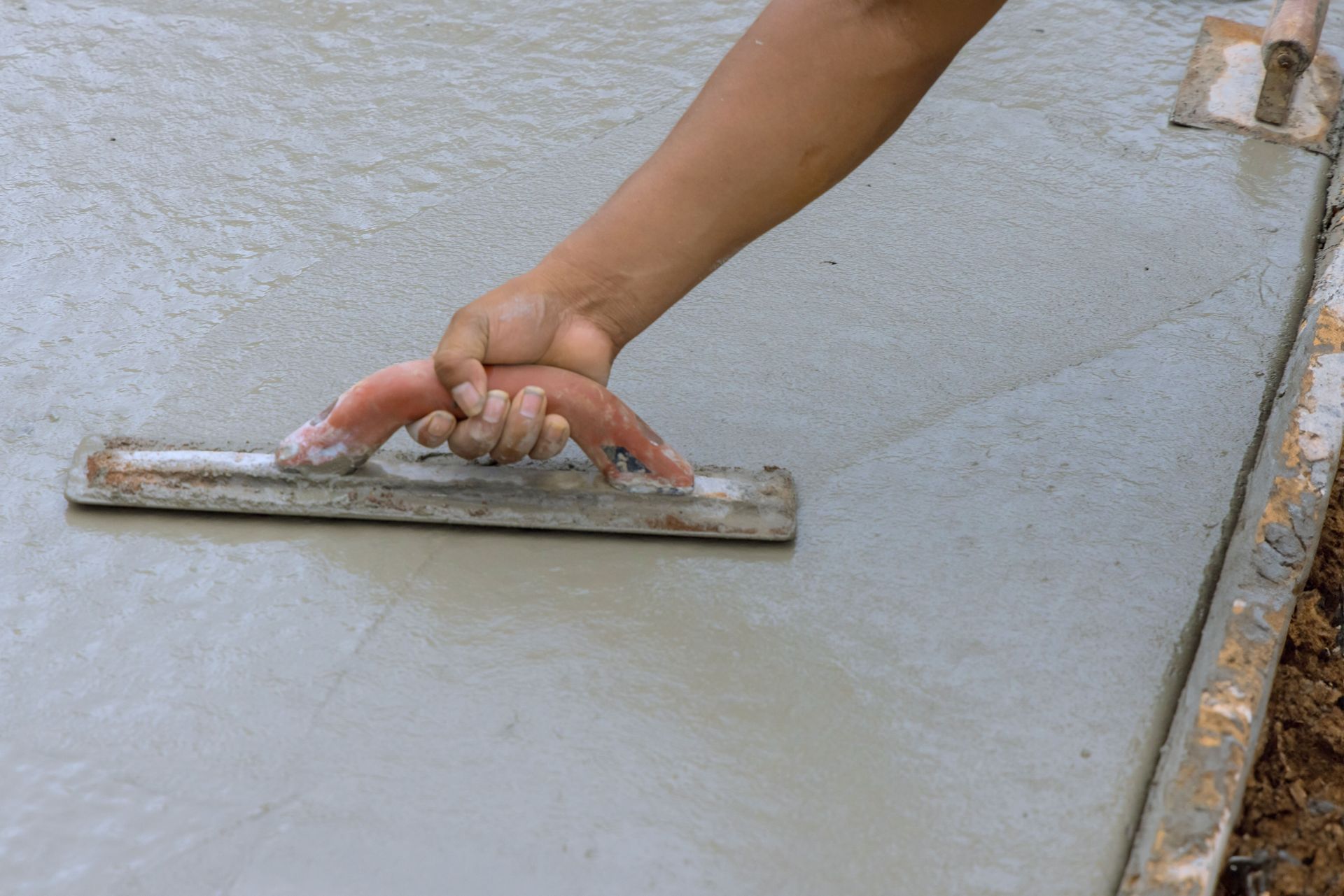 Hand smoothing wet concrete with a trowel on a freshly poured slab
