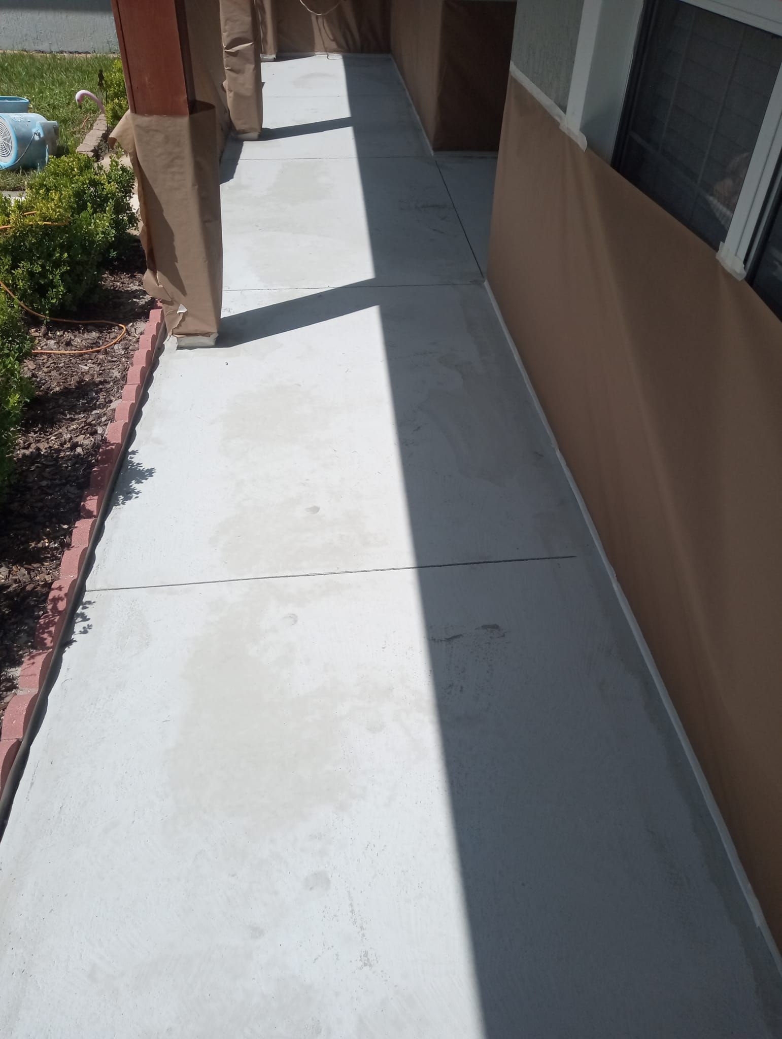 Concrete sidewalk beside tan building with windows and a brick garden border in bright sunlight