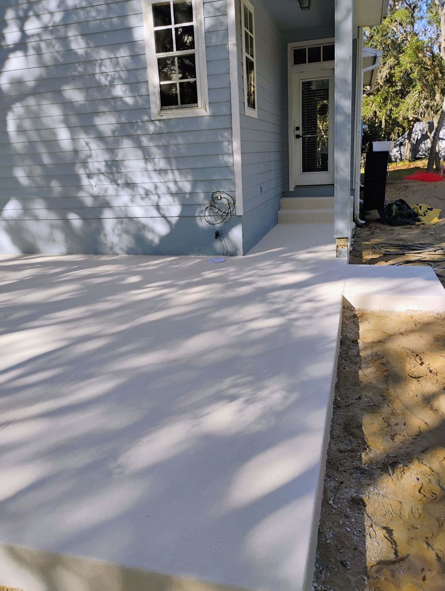 Fresh white concrete walkway beside a light blue house with a front door and window shadows