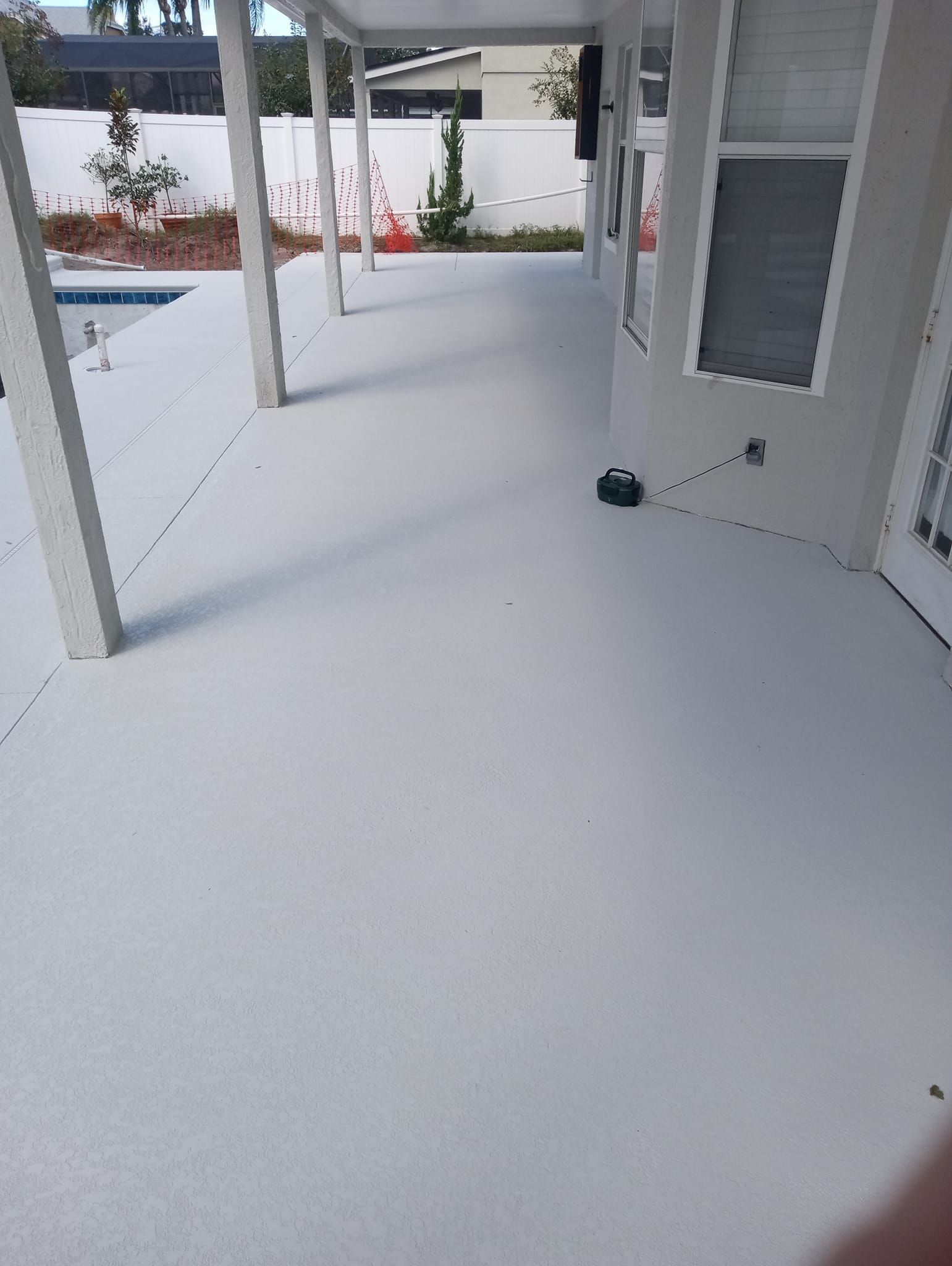 White covered patio with columns, railing, and a door, overlooking a pool and courtyard.