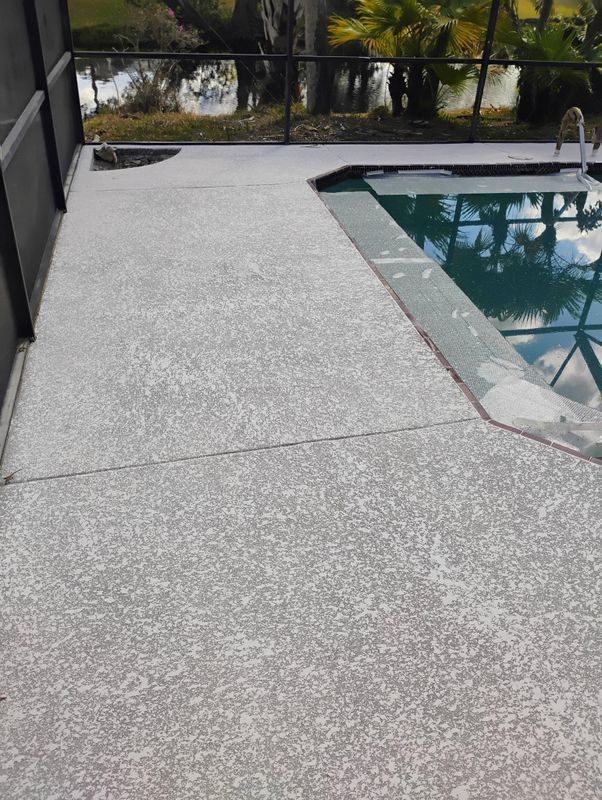 Poolside concrete patio next to a swimming pool with turquoise water and a black fence.