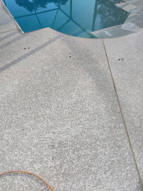 Concrete pool deck beside blue water, with a curved edge and visible seam lines.