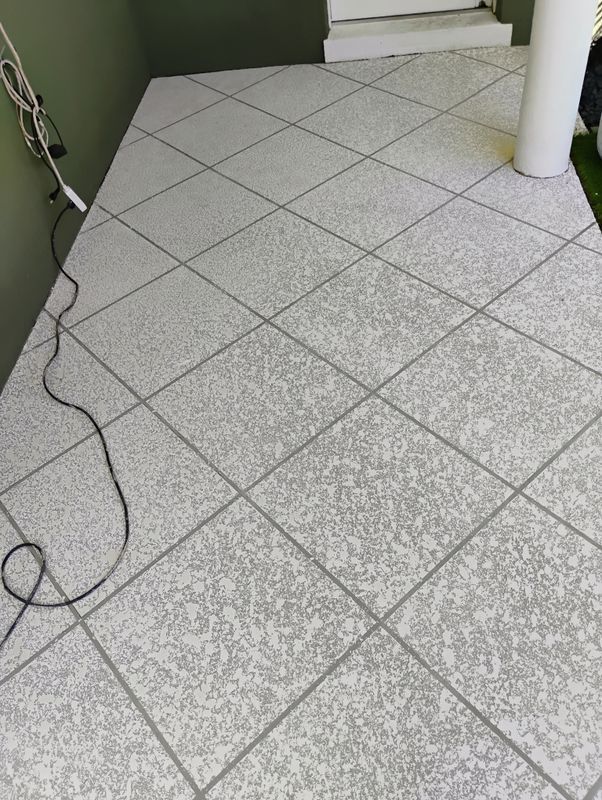 Tiled floor in a hallway with a black cable lying across it, near a wall and pillar