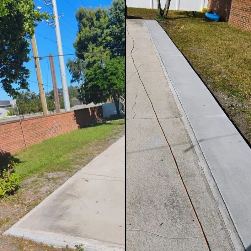 Sidewalk with a cracked seam beside a grassy strip and brick wall under a clear blue sky.