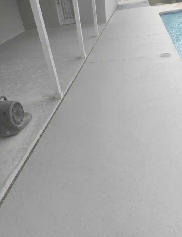 Poolside walkway beside a swimming pool with white columns and gray concrete decking.