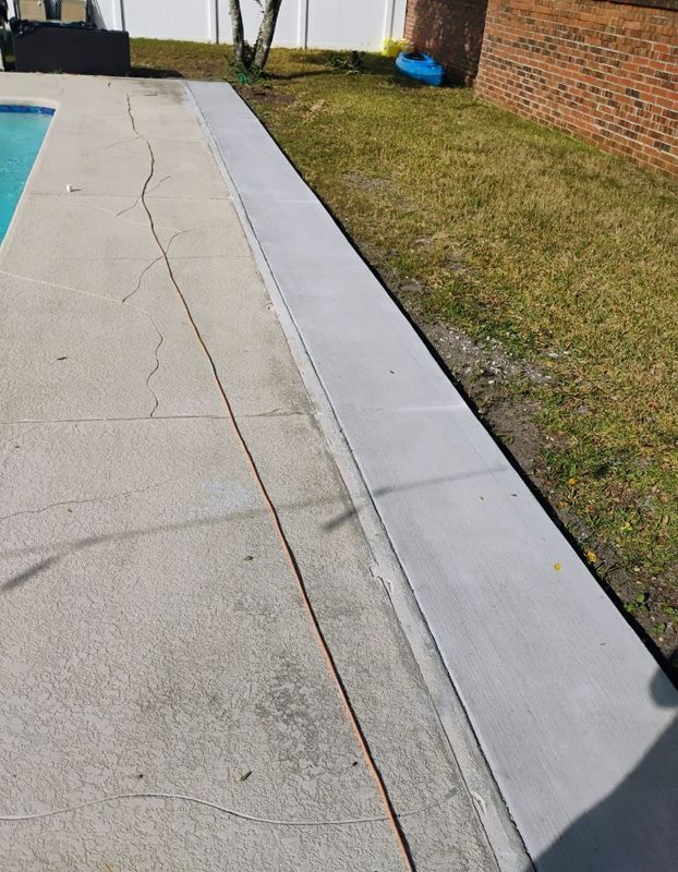 Concrete pool deck beside grass and a brick wall, with a long light-gray edging strip.