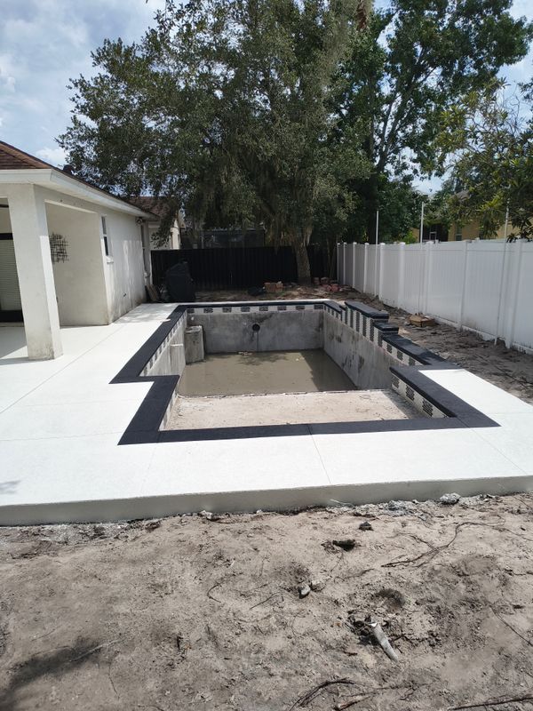 Backyard with empty rectangular pool under construction, white deck, and fence beside a house