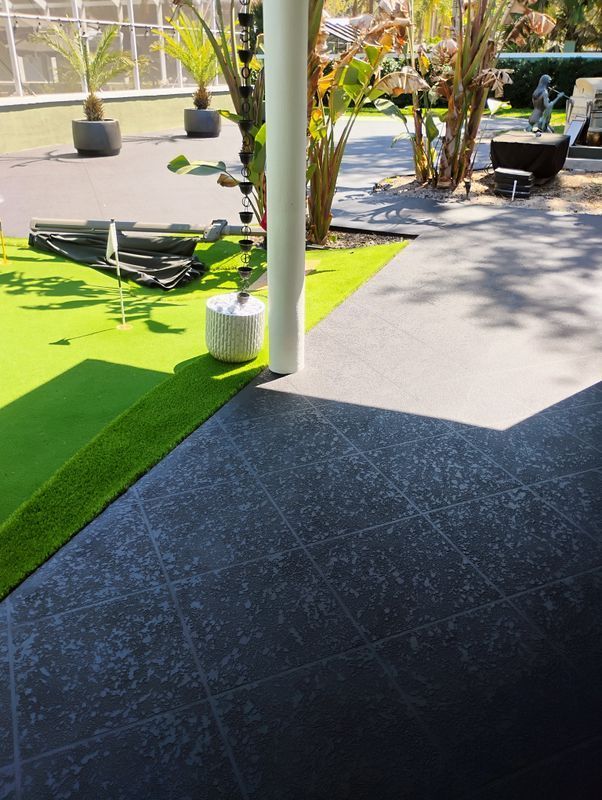 Outdoor patio with black tile floor, green turf, potted plants, and white columns in bright sun