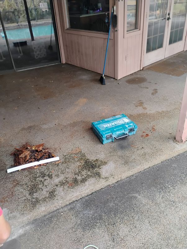 Wet porch with scattered debris, a blue carton, and a broom leaning by the door.