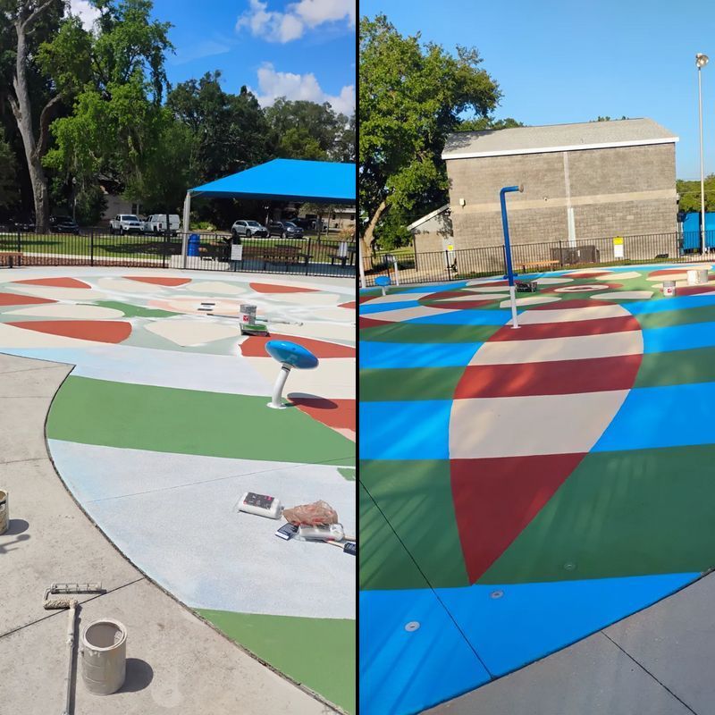 Colorful geometric ground mural under a blue canopy in an outdoor park with trees and a building nearby