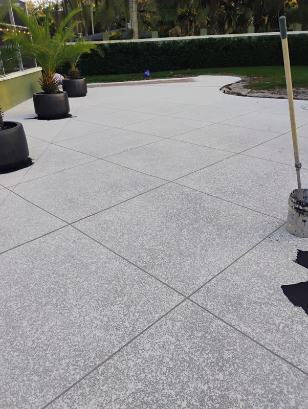 Outdoor patio with light gray tiled flooring, potted plants, and a hedge-lined garden edge