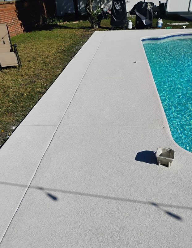 Poolside concrete deck beside blue swimming pool with a small stone near the edge.