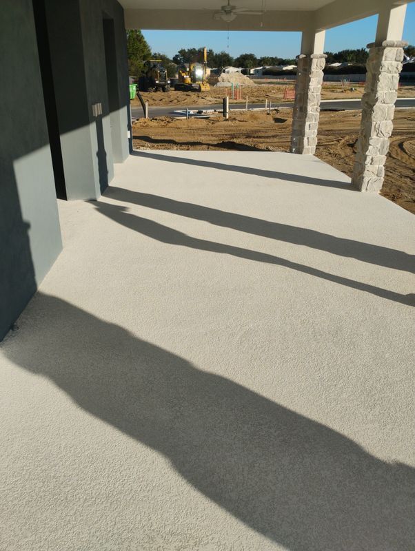 Covered porch with stone columns and long shadows on a concrete floor, overlooking a grassy yard.